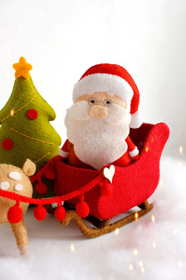 Felt toys - Santa Claus standing near the sleigh, reindeer Rudolph and Christmas tree on the snow, side view