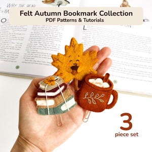 May include: A set of three felt bookmarks featuring an autumn leaf with a face, a stack of books, and a mug with marshmallows. The text reads Felt Autumn Bookmark Collection PDF Patterns & Tutorials and 3 piece set.