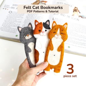 May include: Three felt cat bookmarks in a 3 piece set, featuring grey, calico, and orange tabby designs with stitched details. The text reads Felt Cat Bookmarks PDF Patterns & Tutorial and 3 piece set. These bookmarks are flat, elongated shapes.
