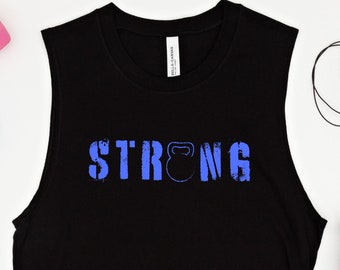 Puede incluir: Camiseta negra sin mangas con la palabra "STRONG" impresa en azul con un gráfico de kettlebell azul. La camiseta está sobre un fondo blanco con una botella de agua, una cuerda para saltar y mancuernas.