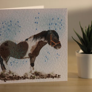 Tarjeta de felicitación en blanco con diseño de pony gitano lluvioso
