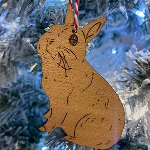May include: A wooden ornament shaped like a rabbit, with a brown woodgrain finish. The ornament is hanging from a red and white string.