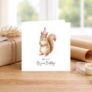 May include: A white square greeting card featuring a brown squirrel illustration wearing a pink polka-dot party hat. The text reads GO NUTS in black and pink, followed by the black script text It's your Birthday! centered below the squirrel.