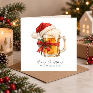 Peut inclure: Une carte de vœux carrée avec une illustration à l'aquarelle d'une chope de bière en verre surmontée d'un bonnet de Père Noël rouge et de mousse blanche. Un ruban rouge avec du houx est noué autour. Le texte indique Merry Christmas TO A SPECIAL DAD.