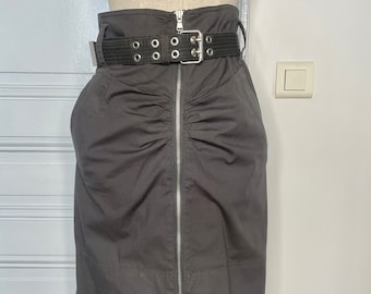 Peut inclure: Jupe gris anthracite avec fermeture éclair avant et ceinture noire à boucle argentée. La jupe est taille haute et froncée. La ceinture a des oeillets argentés.