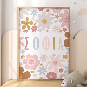 May include: A framed floral print with the name "ΣΟΦΙΑ" in pastel colors. The artwork features a variety of flowers in pink, yellow, and brown, set against a white background. The frame is a light wood color.