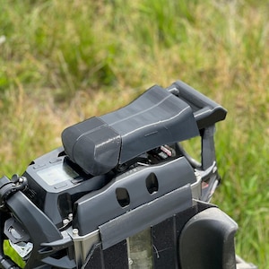 Könnte beinhalten: Ein schwarzes elektrisches Einrad mit Sitz und Griff. Das Einrad hat ein digitales Display und ist für den Offroad-Einsatz konzipiert. Der Hintergrund ist verschwommenes grünes Gras.