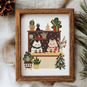 Könnte beinhalten: Ein gerahmtes Kreuzstichbild mit zwei Katzen in einer festlichen Szene. Die Katzen tragen Schals und sind von kleinen Weihnachtsbäumen und Topfpflanzen umgeben. Ideal für die Weihnachtsdekoration.