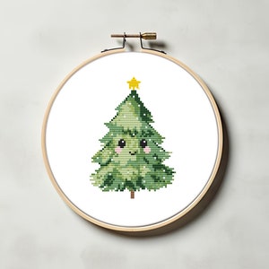 May include: A green cross-stitch Christmas tree with a yellow star on top and a smiling face. The tree is in a wooden embroidery hoop.