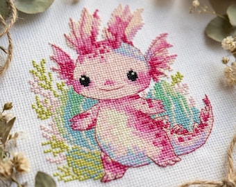 May include: A cross-stitch design of a smiling axolotl in pink, white, and blue hues. The axolotl is surrounded by green and pink floral accents, all stitched on white fabric. The design has a cute, cartoonish style.