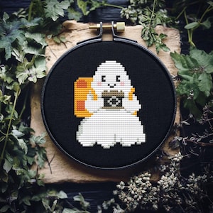 May include: A white ghost with a friendly face holding a small orange and black pumpkin. The ghost is embroidered on a black fabric background.