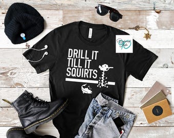 May include: Black t-shirt with white text that reads "Drill it till it squirts" and a graphic of a drill bit going through a fish.