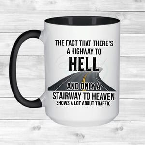 Può includere: Tazza in ceramica bianca con manico e interno neri. La tazza presenta il testo "THE FACT THAT THERE'S A HIGHWAY TO HELL AND ONLY A STAIRWAY TO HEAVEN SHOWS A LOT ABOUT TRAFFIC" con una grafica stradale.