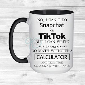 May include: White ceramic mug with a black handle and interior. The mug features text that reads, "NO, I CAN'T DO Snapchat OR TikTok BUT I CAN WRITE in cursive DO MATH WITHOUT A CALCULATOR AND TELL TIME ON A CLOCK WITH HANDS."