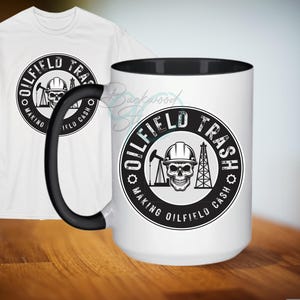 Puede incluir: Una taza de cerámica blanca con un borde y un asa negros. La taza tiene un gráfico en blanco y negro de una calavera con un casco y el texto "Oilfield Trash Making Oilfield Cash".