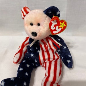 Pode incluir: Um peluche Beanie Baby de pelúcia com tema da bandeira americana, vermelho, branco e azul, com uma etiqueta Ty que diz "Beanie Original Baby".