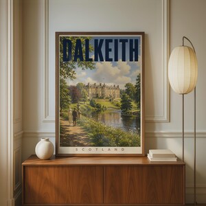 May include: A framed travel poster featuring a landscape illustration of Dalkeith, Scotland. The print displays a large stone building, a river, and two figures walking on a path, with the text DALKEITH and SCOTLAND printed in dark blue and black.