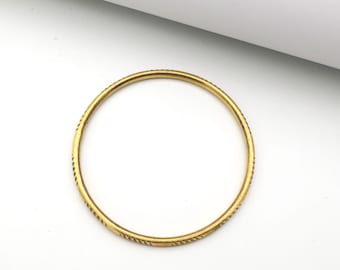 Puede incluir: Una pulsera tipo brazalete circular y delgada de oro, con un patrón repetitivo de líneas diagonales grabadas a lo largo de toda su superficie exterior. El metal tiene un acabado pulido, creando un tono dorado uniforme en todo el aro.