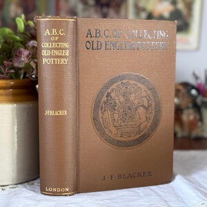 May include: A brown hardcover book titled A.B.C. of Collecting Old English Pottery by J.F. Blacker. The front cover features a circular emblem with a crest, and the spine displays the title, author, and the location London in gold lettering.