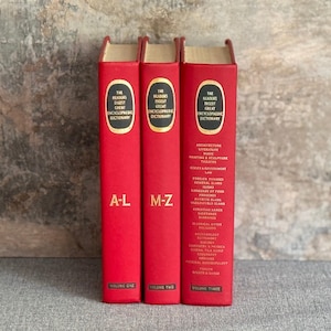 May include: Three red hardcover books titled "The Reader's Digest Great Encyclopedic Dictionary." Volume one is labeled A-L, volume two M-Z, and volume three lists topics. The books have gold lettering and are displayed on a neutral background.