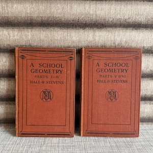 May include: Two antique books titled "A School Geometry" by Hall & Stevens. The books are a reddish-brown colour with black text and decorative borders. The first book is labelled "Parts 1-IV" and the second "Parts V & VI".