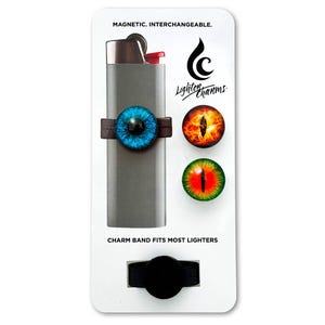 May include: A set of three magnetic eye-themed lighter charms. The charms are blue, orange, and green. The charms are attached to a black band that fits most lighters. The text on the card reads "Magnetic. Interchangeable. Lighter Charms. Charm band fits most lighters."
