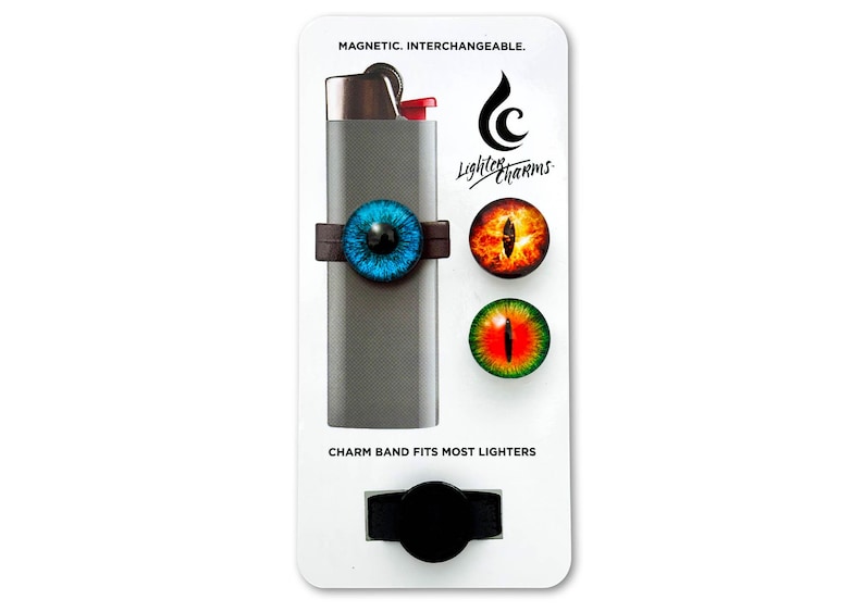 May include: A set of three magnetic eye-themed lighter charms. The charms are blue, orange, and green. The charms are attached to a black band that fits most lighters. The text on the card reads "Magnetic. Interchangeable. Lighter Charms. Charm band fits most lighters."