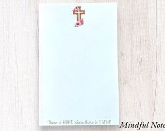 May include: A white notepad with a brown wooden cross and pink flowers at the top. The notepad has the text "There is HOPE where there is FAITH!" at the bottom and the words "Mindful Notes" in the lower right corner.