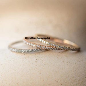 Pode incluir: Três anéis delicados de ouro e prata com uma fileira de pequenos diamantes engastados em cada banda. Os anéis estão empilhados um em cima do outro.