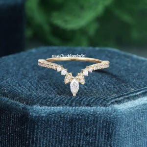 Può includere: Un delicato anello d'oro con un diamante a forma di marquise al centro e diamanti più piccoli incastonati in una fascia curva. L'anello è su una superficie di velluto blu.