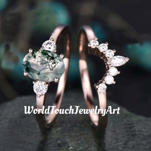 Könnte beinhalten: Zwei roségoldene Ringe. Ein Ring hat einen großen ovalen Moosachatstein mit kleineren Akzentsteinen. Der andere Ring hat ein geschwungenes Design mit mehreren runden und marquiseförmigen weißen Steinen. Der Text "WorldTouchJewelryArt" ist sichtbar.