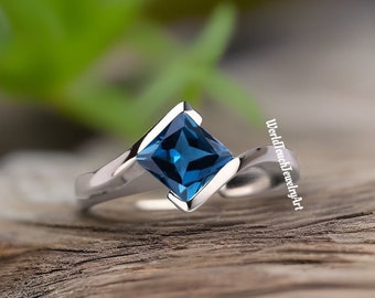 May include: A silver ring featuring a square blue topaz gemstone. The ring has a twisted band.