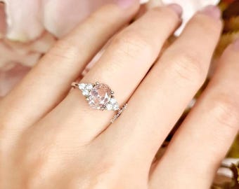 May include: A silver ring with a large oval-shaped pink gemstone surrounded by smaller clear gemstones.