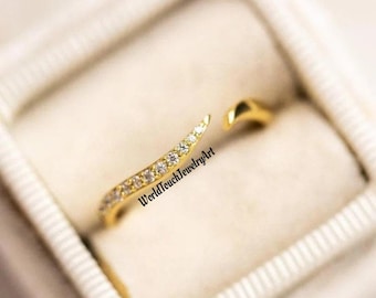 May include: A gold ring with a curved design and small clear stones. The ring is open on one side and has a pointed end.