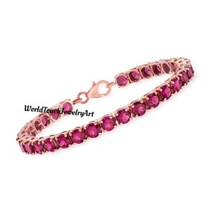 Puede incluir: Pulsera de oro rosa con una fila de gemas rojas vibrantes. La pulsera tiene un diseño delicado y un cierre seguro. El texto "WorldTouchJewelryArt" es visible en la imagen.