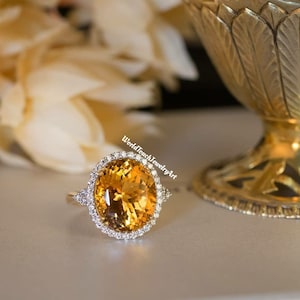 以下が含まれることがあります： 大きな楕円形のトパーズの宝石を、小さなダイヤモンドのハローで囲んだ金のリング。リングは白い金属のバンドにセットされています。