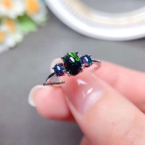 Può includere: Un anello d'argento con tre pietre preziose di opale nero. La pietra centrale è più grande delle due pietre laterali.