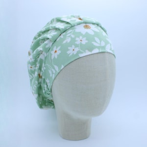 May include: A green and white floral print turban style hat. The hat is made of a soft, stretchy fabric and has a gathered look.
