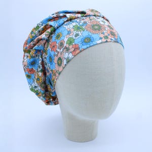 May include: A floral patterned turban headband in shades of blue, pink, and green. The headband is made of a soft, stretchy fabric and is designed to be worn comfortably.