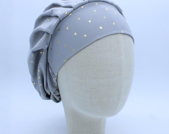 May include: A gray satin sleep cap with a gold heart pattern. The cap is designed to protect hair while sleeping.
