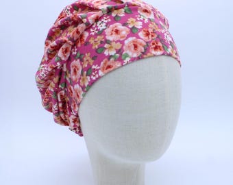 Könnte beinhalten: Eine rosafarbene Turbanmütze mit floralem Muster. Die Mütze ist aus weichem, dehnbarem Stoff und hat einen gerafften Look.