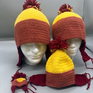May include: Handmade crochet hats in yellow and brown with ear flaps and a pom-pom on top. The hats are displayed on mannequin heads. A matching scarf and keychain are also included in the image.