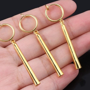 May include: Three gold-colored clip-on earrings with long, straight, cylindrical dangles.