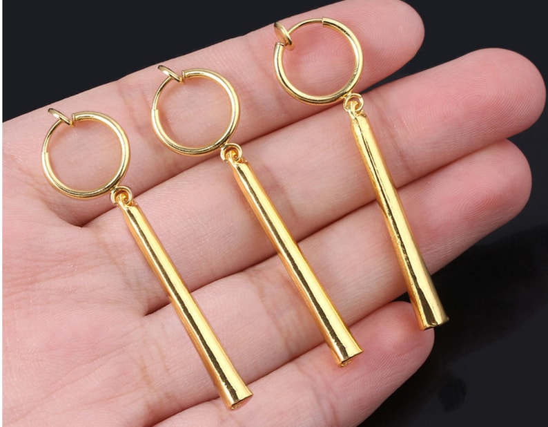 May include: Three gold-colored clip-on earrings with long, straight, cylindrical dangles.