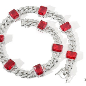 May include: A silver-colored chain necklace with large, rectangular red gemstones. The chain links are encrusted with small, clear stones. The necklace is displayed on a white background. The Jewelry Junction logo is in the bottom right corner.