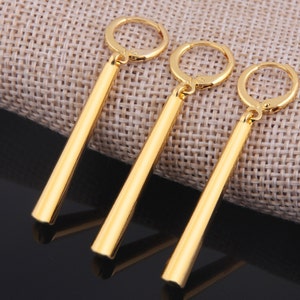 May include: Three gold-colored dangle earrings with a long, thin, cylindrical design. The earrings have a hoop closure.