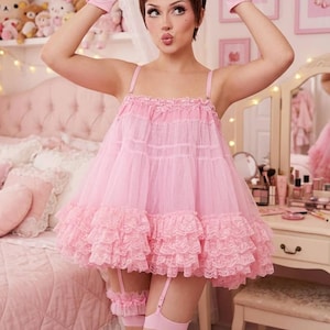 Può includere: Un abito babydoll rosa chiaro con corpetto arricciato e orlo in pizzo a balze. L'outfit include un grande fiocco per capelli rosa abbinato con stampa a margherite, guanti rosa chiaro, reggicalze e sandali con tacco rosa in pelliccia.