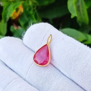Op de afbeelding: Een druppelvormige hanger met een gefacetteerde roze edelsteen in een goudkleurige metalen zetting. De hanger is voorzien van een klein rond oogje aan de bovenzijde voor bevestiging en heeft een gepolijste afwerking met een roze kleur.