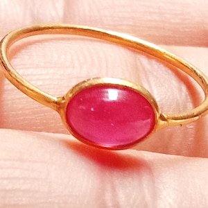 May include: A gold ring with a bright pink oval gemstone.