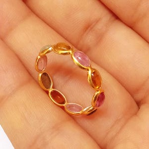 May include: A gold ring with a band of oval-shaped gemstones in various shades of pink, orange, and brown.